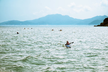 A group of unrecognizable people in kayaks moving on sea water near Hong Kong coastline. Island mountains in haze on background. Weekend activities. Extreme hobby and leisure of active men and women.