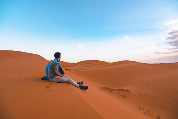 Young traveler man resting on a dune in the Sahara Desert