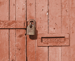 close up of an old brown wooden door with faded paint and a rusty closed padlock and old metal letterbox