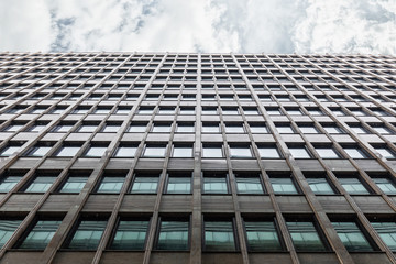 The Facade Of The Office Building Shot From The Bottom Up With A Horizontal Strip Of Gray Sky With Clouds. The Windows Of The Business Center Reflects The Adjacent Building