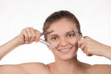 Young girl pulls out her eyebrows with tweezers metal on a white background