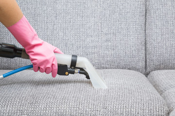 Dry cleaner's employee hand in protective rubber glove cleaning sofa with professionally extraction...