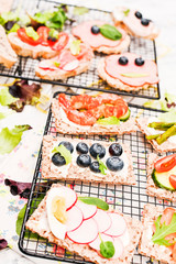 Different sandwiches for breakfast on a white wooden background. Crackers with prawns, vegetables, cheese and ham.