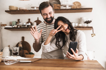 Portrait of smiling couple hugging together and holding smartphone while cooking in kitchen at home