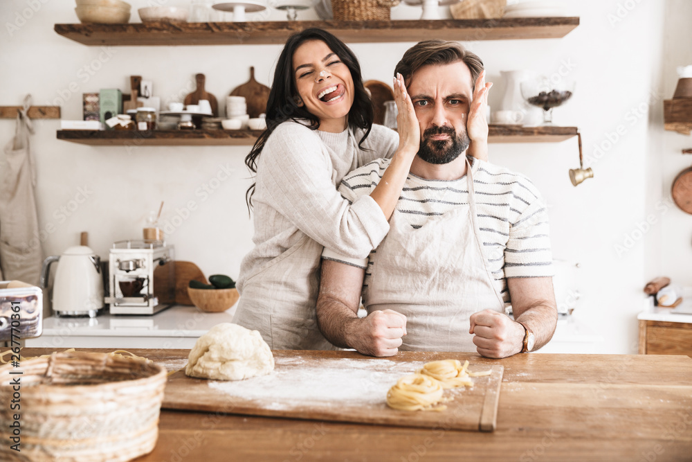 Wall mural Image of amusing couple having fun together while making homemade pasta in kitchen at home