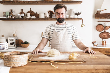 Portrait of serious brunette man making homemade pasta of dough in kitchen at home
