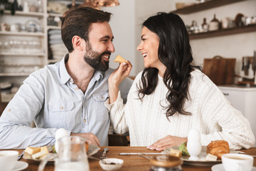 Portrait of attractive brunette couple eating together at table while having breakfast in kitchen at home