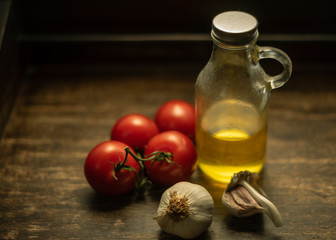 Garlic, vine tomatoes and glass bottle with oil on wooden vintage background.