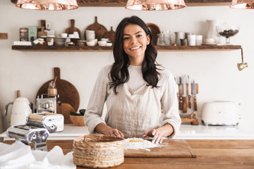 Portrait of smiling woman cooking pastry with flour and eggs in kitchen at home