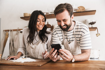 Portrait of happy couple reading recipe while cooking pastry with flour and eggs in kitchen at home