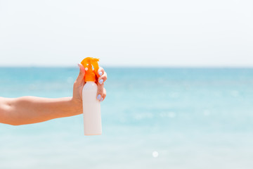 Croped image of woman's hand holding sunscreen spray at the sea background