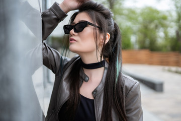 Beautiful asian girl in sunglasses stands against a gray marble wall. Not looking at the camera. Close portrait portrait.