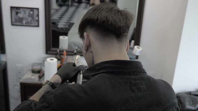 Barber style. Male barber in plaid shirt combing hair of a male client at barbershop Attractive professional hairdresser working at his barbershop styling hair of his client young handsome man 