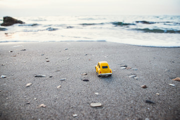 Vacation and travel concept. Yellow toy car on the beach in the sunlight in summer