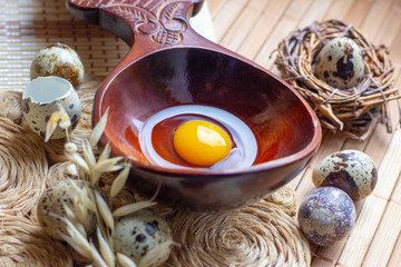 Fresh raw quail eggs in wooden spoon on rustic straw and wooden vintage background.
