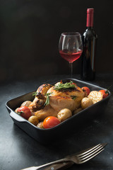 Roasted chicken with potatoes, glass of wine on black table in interior.