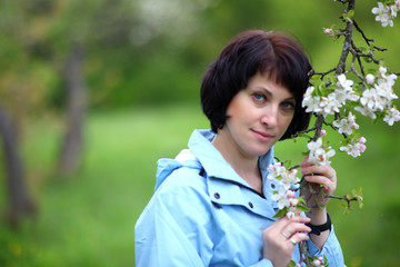 Obraz premium Beautiful mature woman posing for the camera in the spring garden. The girl enjoys the flowering of apple trees.