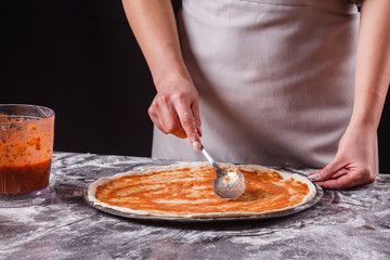 young woman in a gray aprong prepares a pepperoni pizza