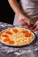 young woman in a gray aprong prepares a pepperoni pizza