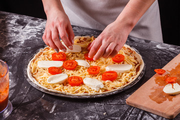 Obraz na płótnie Canvas young woman in a gray aprong prepares a pizza margarita
