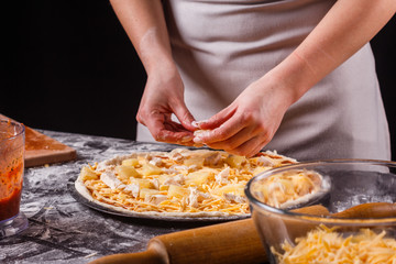 young woman in a gray aprons prepares a Hawaiian pizza
