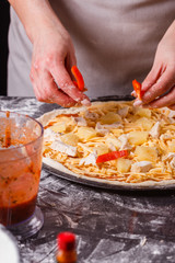 young woman in a gray aprons prepares a Hawaiian pizza