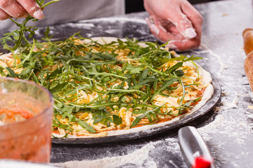 young woman in a gray aprong prepares a vegetarian pizza