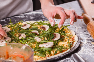 young woman in a gray aprong prepares a vegetarian pizza