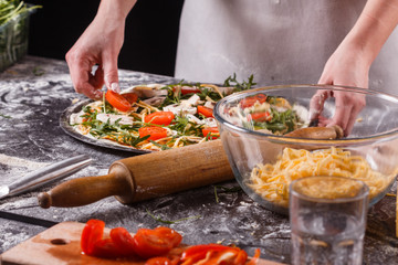 young woman in a gray aprong prepares a vegetarian pizza
