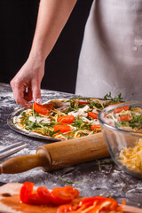 young woman in a gray aprong prepares a vegetarian pizza
