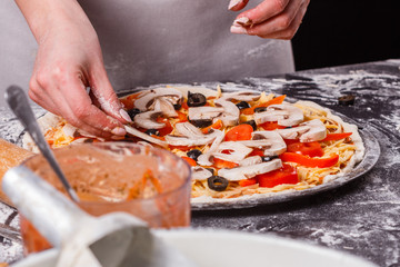 young woman in a gray aprong prepares a vegetarian pizza