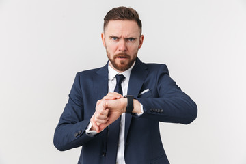 Serious young handsome businessman posing isolated over white wall background looking at watch.