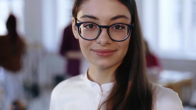 Close-up portrait, happy young brunette design professional business woman in eyeglasses smiling at camera at office.