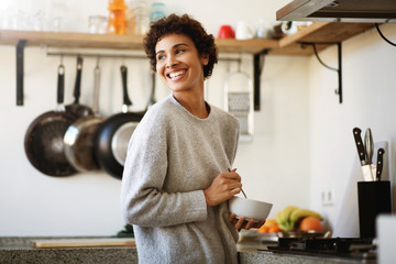 happy young african american woman with cereal bowl in kitchen