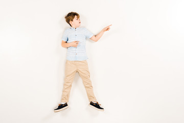 top view of surprised kid pointing with finger while lying on white