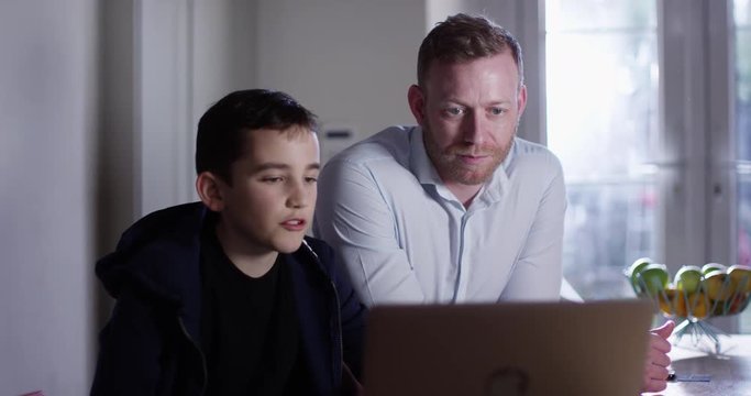 4K Dad & son spending time together at home & streaming a movie on laptop. Slow motion.