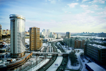 Novosibirsk cityscapes, high rise office and residential buildings and skyscrapers in city, road for cars and pedestrian bridge, top view in winter