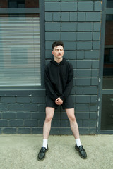 young brunette with bright features, big eyes and plump lips with a fashionable haircut and thick curly black hair in a black hoodie, black shorts, black shoes and white socks on a gray background