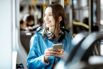 Young stylish woman using public transport, sitting with phone and headphones in the modern tram
