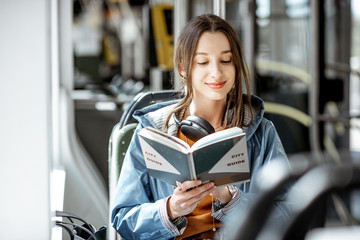 Young woman reading book while moving in the modern tram, happy passenger at the public transport