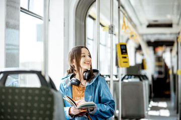 Young woman reading book while moving in the modern tram, happy passenger at the public transport