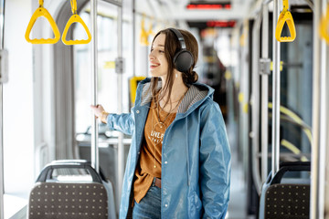 Young stylish woman with headphones while moving in the modern tram. Happy passenger enjoying trip...