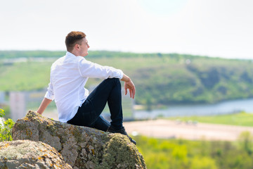 Naklejka na ściany i meble Attractive smart man sitting relaxing on a rock