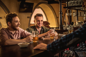 Cheerful friends drinking draft beer in a pub