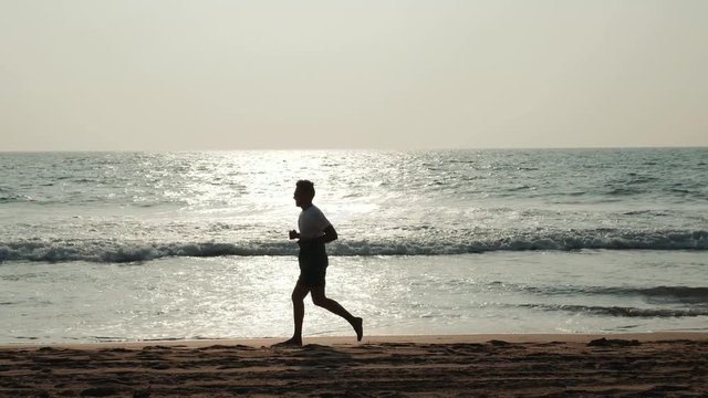 silhouette student tourist young athlete runner man with fit strong body training on beautiful Summer sunset beach sand running barefoot in sport well being and healthy lifestyle concept