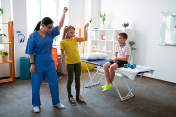 Active light haired girl raising hand with yellow resistance rope
