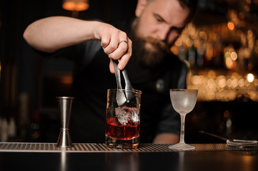 Bartender puts ice cube in alcohol cocktail