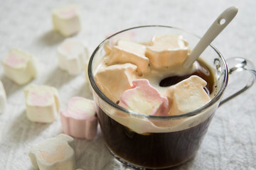 Black coffee in transparent cup with marshmallows on white