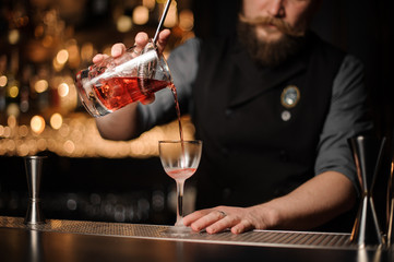 Male bartender pours alcohol cocktail with strainer