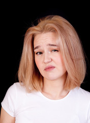 Portrait of a young blonde woman in a white T-shirt on a black background looking contemptuously and appreciatively. Concept emotion appreciation and contempt